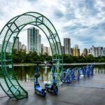 Scooters parked among urban art installations by a lake in Londrina, Brazil.