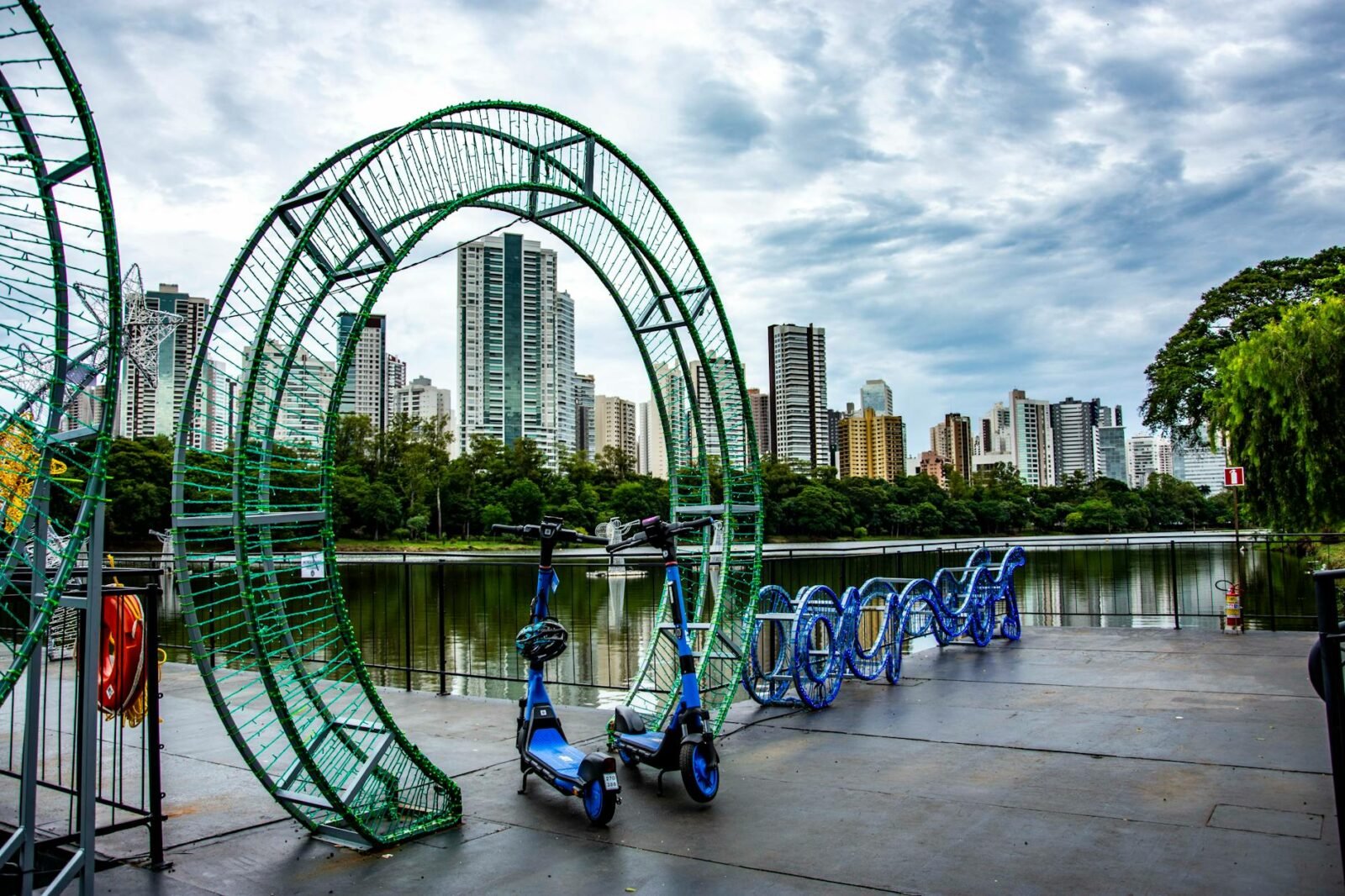 Scooters parked among urban art installations by a lake in Londrina, Brazil.