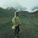 Man wearing raincoat hiking through scenic Juta mountains in Georgia on a misty day.