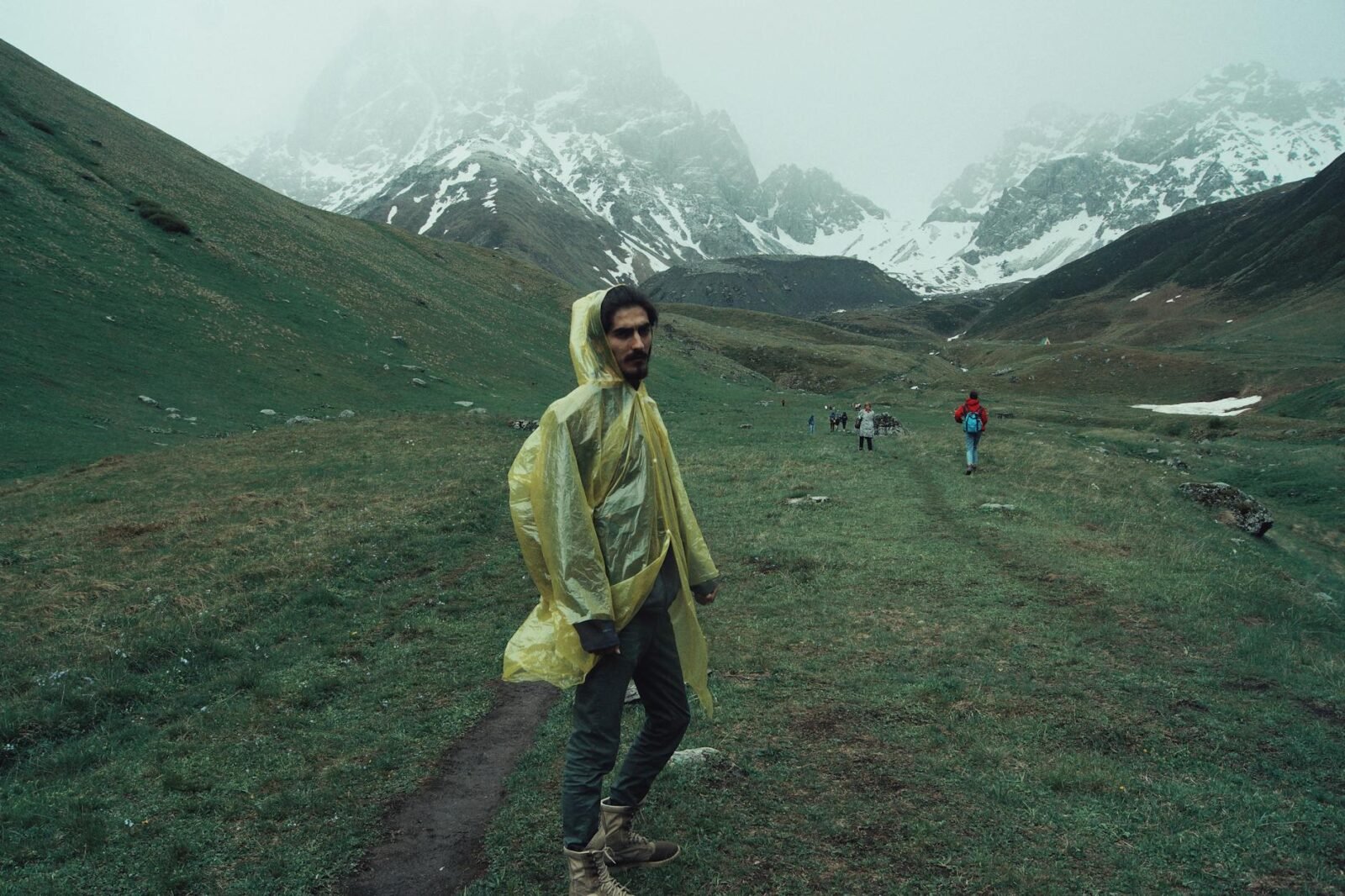 Man wearing raincoat hiking through scenic Juta mountains in Georgia on a misty day.