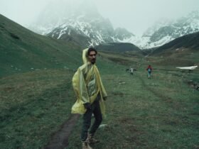 Man wearing raincoat hiking through scenic Juta mountains in Georgia on a misty day.